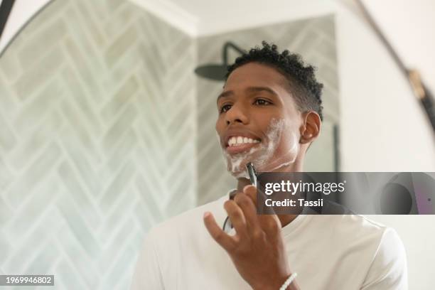 happy man, shave and grooming in mirror for beard trim, hygiene or facial treatment in bathroom at home. face of young african male person smile and shaving for skincare, cleaning or beauty at house - male hair removal stockfoto's en -beelden