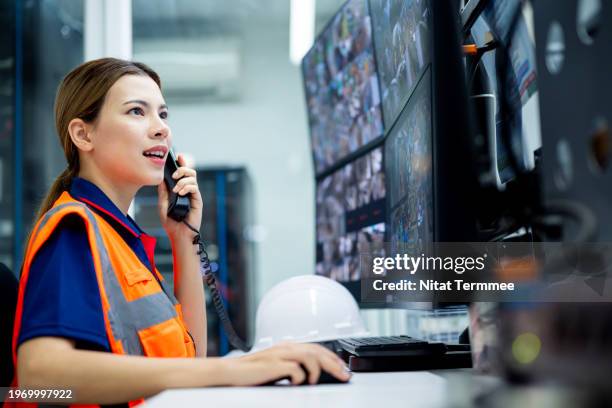 video surveillance system help with workflow monitoring in the manufacturing process. side view a female security office discuss on phone during alarm and alert from security camera in the control room of the manufacturing facility. - defender actividad fotografías e imágenes de stock