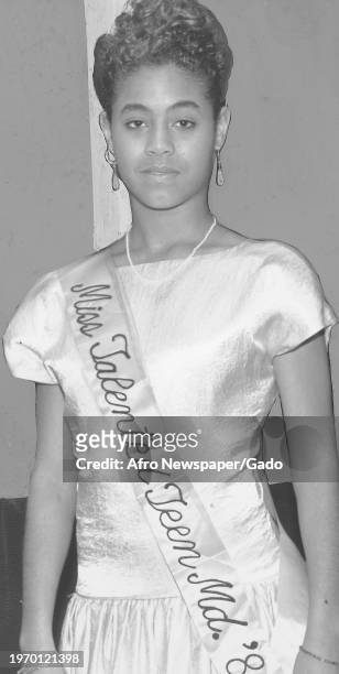 Mid shot of Jada Pinkett facing the camera with a relaxed expression, wearing a formal gown and a "Miss Talented Teen Md '88" sash, participating in...