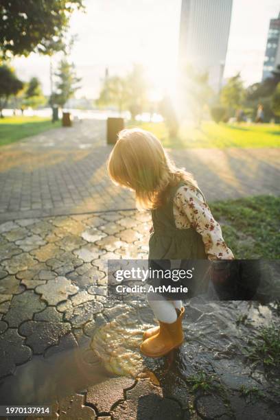 little girl in rubber boots playing in puddles after rain in springtime or autumn - girl wearing boots stock pictures, royalty-free photos & images