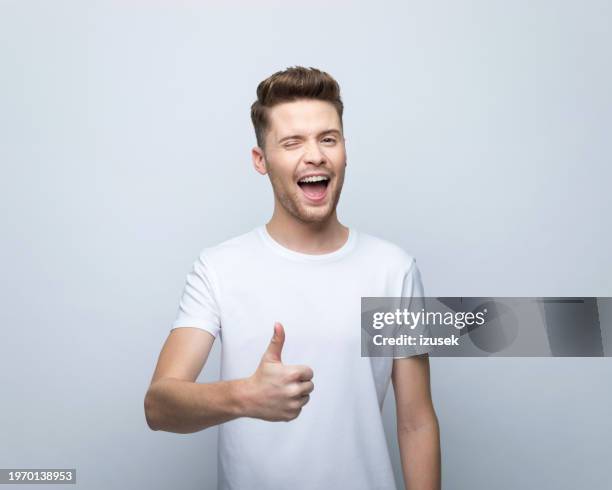 portrait of young man with thumb up - zwinkern stock-fotos und bilder