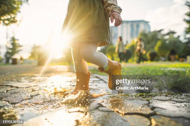 little girl in rubber boots playing in puddles after rain in springtime or autumn - puddle stock pictures, royalty-free photos & images