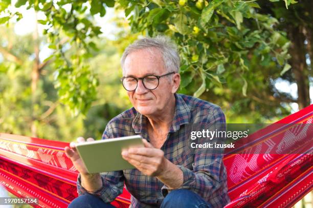 senior man wearing eyeglasses sitting on hammock - man on hammock stock pictures, royalty-free photos & images