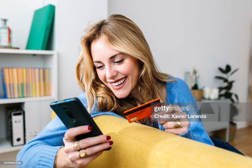 Happy young woman holding credit card while shopping online at home