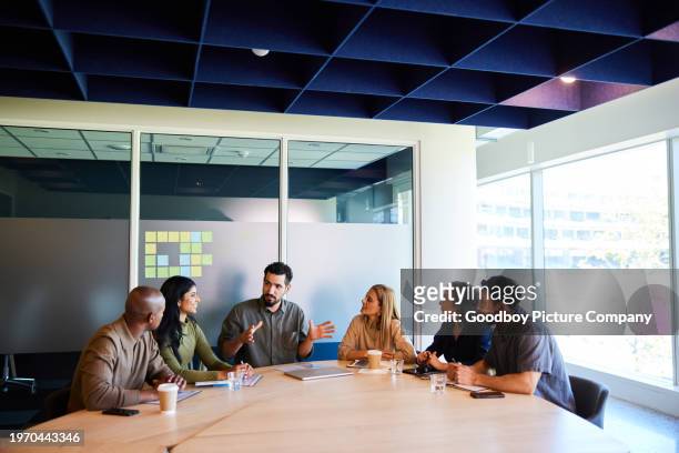 businessman talking to diverse colleagues during a meeting in an office board room - multi ethnic business people having discussion at table in board room stockfoto's en -beelden