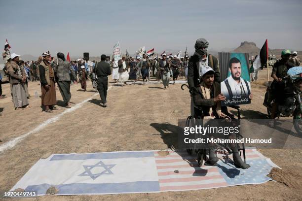 Man pushes a Houthi disabled fighter sitting on a wheelchair stepping over U.S. And Israeli flags during a weaponized rally and parade against the...