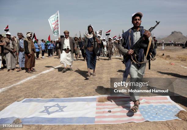 Houthi fighters lift rifles, Yemen and Palestine flags, and Houthi emblems march during a weaponized rally and parade against the America-Britain...