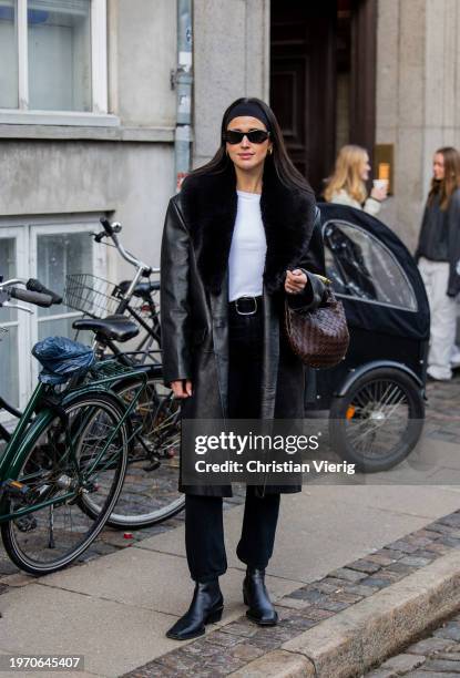 Darja Barannik wears Bottega Veneta bag, hair band, black shearling coat, white shirt, black belted pants, sunglasses, ankle boots outside Nicklas...