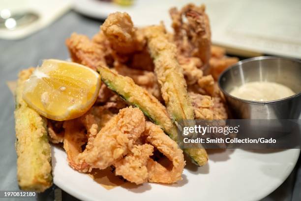 Fried calamari with a slice of lemon and a side of dipping sauce on a white plate at an Eataly restaurant, San Jose, California, December 23, 2023.