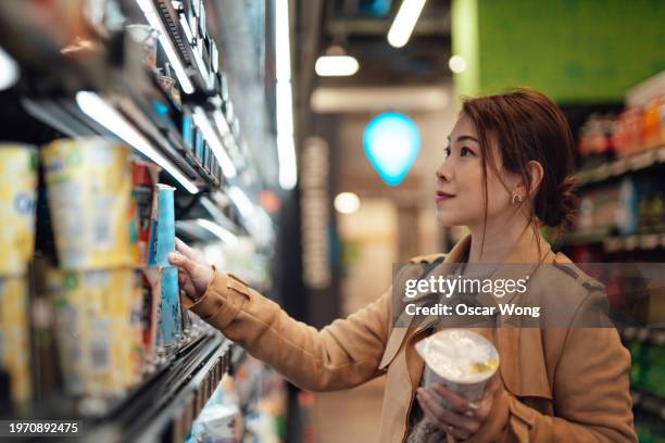 young asian woman choosing yoghurt from the shelves at supermarket. - joghurtbecher stock-fotos und bilder