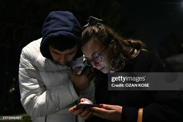 Relatives of hostages watch on their smartphone a live broadcast made by the assailant who took an undisclosed number of people hostage inside a...