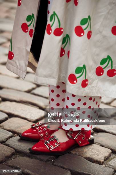 Anais Van Oekel is wearing a white top, white pants with red dots, beige coat with red cherries, red Ganni shoes, and a red wool hat during the...