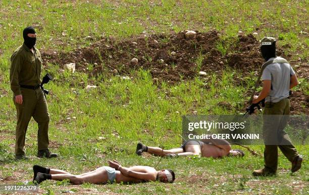 Cuffed, stripped and blindfolded Palestinian suspects are guarded by Israeli security as they lie in a field after their mini van was intercepted by...