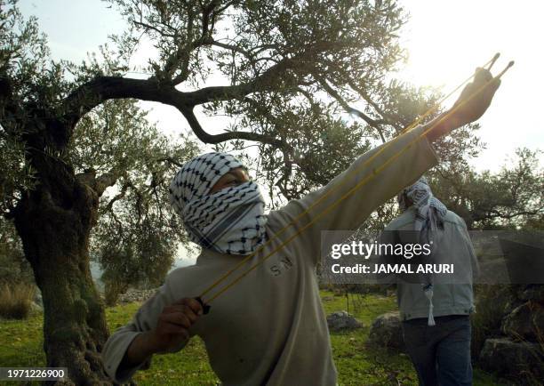 Masked Palestinian demonstrator uses a sling shot to hurl stones at Israeli soldiers during the weekly protest against the construction of Israel's...
