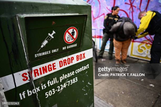 Syringe drop box stands on the street as a Portland Police officer conducts an investigation into drug dealing and issues a citation for drug...