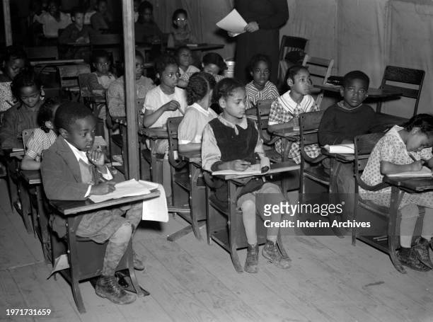 View of a group of young African American students seated in a makeshift classroom at Tent City near Shawneetown, Illiniois, April 1937. Tent City,...