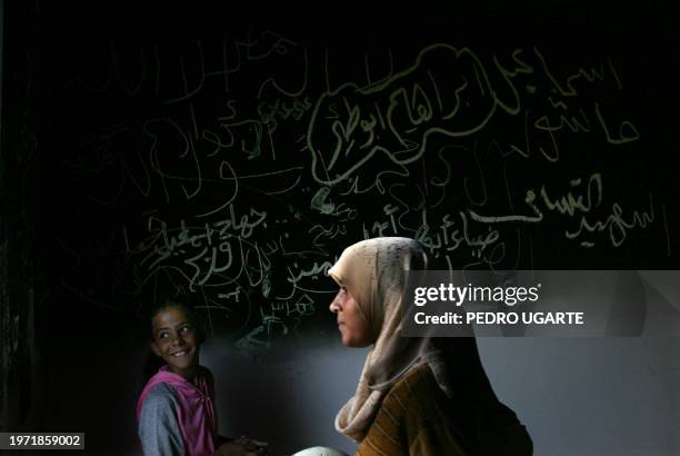 Palestinian girls walk past Arabic graffiti of the names of Palestinians killed during the intifada written on a wall inside the abandoned synagogue...