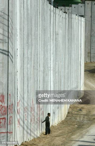 Palestinian boy walks next to the controversial Israeli "security barrier" which splits the West Bank village of Abu Dis into two, on the edge of...