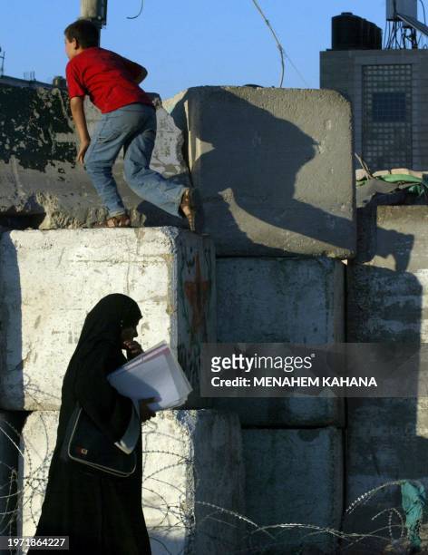 Palestinian boy climbs on the concrete wall separating Jerusalem from the west Bank village of Abu Dis 29 June 2003 as a Palestinian woman passes by....