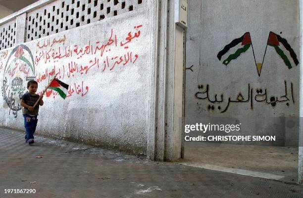 Little palestinian boy carries a Palestinian flag as he walks past a grafitti-covered wall in Rafah 15 November 2000. Palestinian leader Yasser...