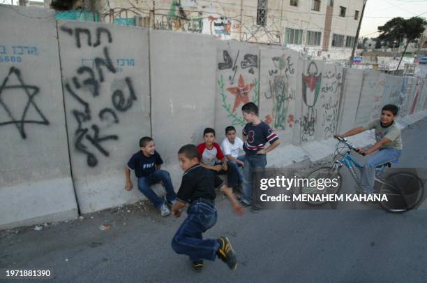 Palestinian children play next to the concrete wall separating east Jerusalem from the West Bank village of Abu Dis 29 June 2003. US national...