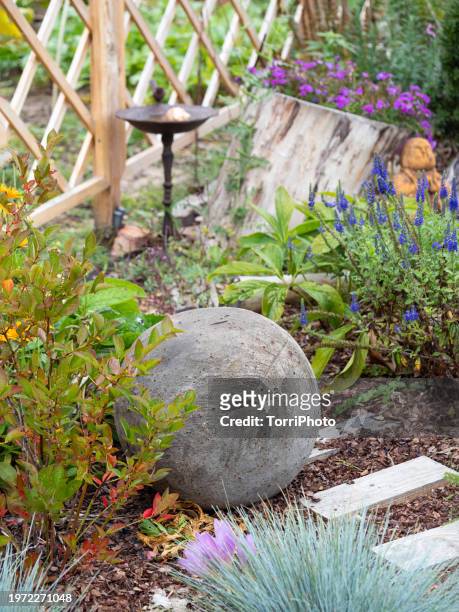 close-up of a cement ball with an imprint of a fern leaf lying on a flowerbed among flowers and garden plants. garden decor. concrete sculpture - arredamento da giardino foto e immagini stock