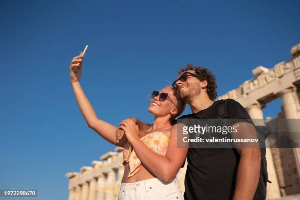 young couple travelers taking selfie in front of background in acropolis in athens, greece - art of the vintage selfie stockfoto's en -beelden