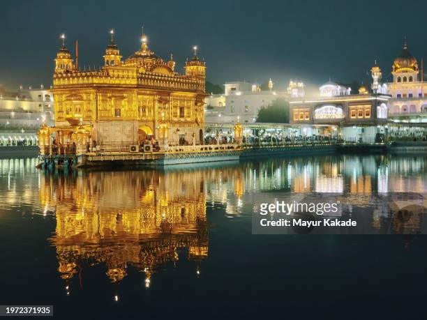 nighttime majestic glow of golden temple, amritsar with reflections in the water - amritsar stock-fotos und bilder