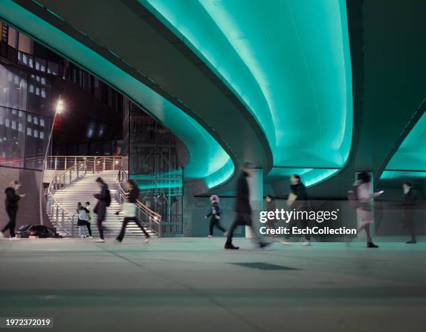 evening commute with people passing a led illuminated viaduct at a modern business district - azul turquesa imagens e fotografias de stock