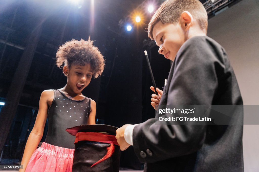 Child magician boy doing magics with the assistant on performance at stage theater