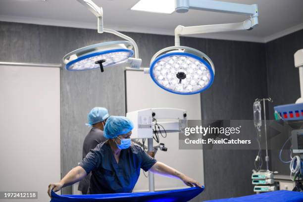 krankenschwester deckt op-tisch mit op-tuch ab - operationstisch stock-fotos und bilder