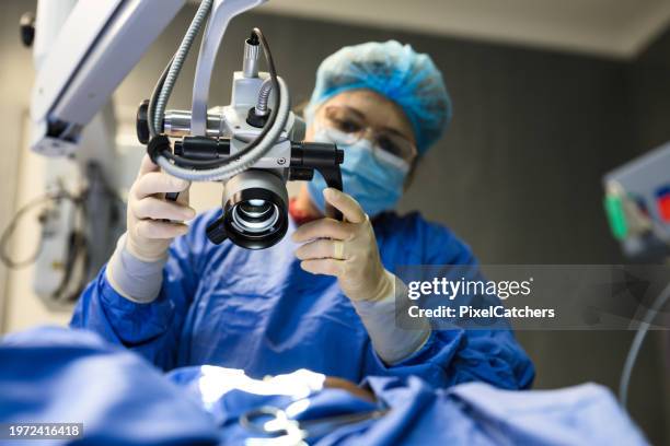 female doctor positioning microscope in operating theatre - hospital equipment stock pictures, royalty-free photos & images