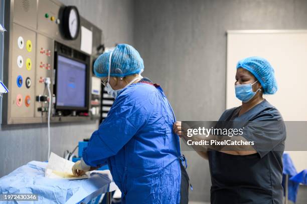 nurse fastening operating gown assisting doctor to get dressed - ropa de operar fotografías e imágenes de stock