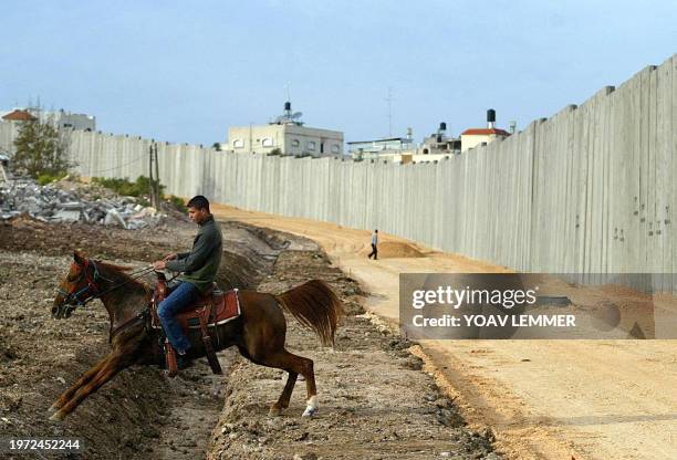 Palestinian from the West Bank village of Nazlat Issa jumps with his horse over a trench 02 January 2004, next to a concrete section of the Israeli...