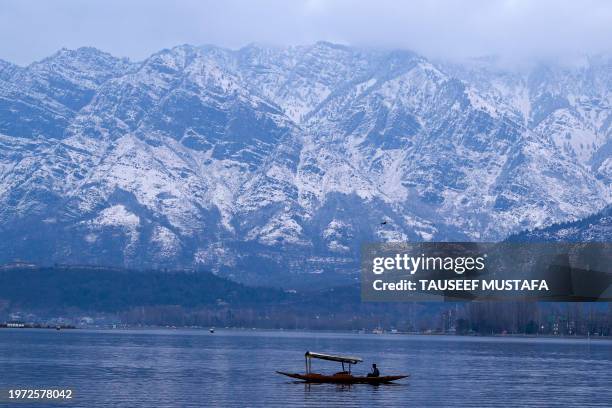 Man rows a boat at Dal Lake against the snow laden mountains in Srinagar on February 2, 2024.