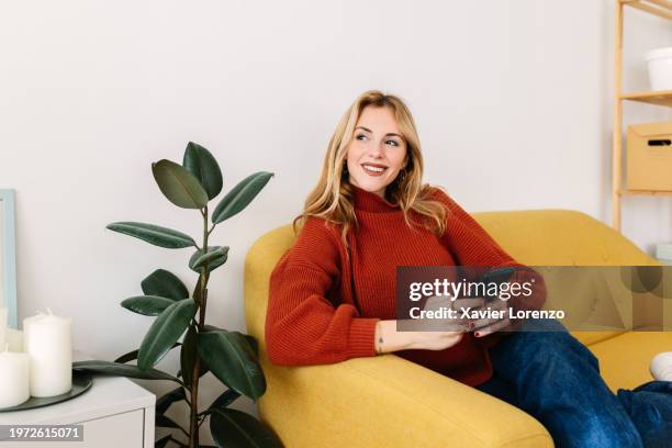 happy beautiful young woman with mobile phone resting on couch at home - nuria stock pictures, royalty-free photos & images