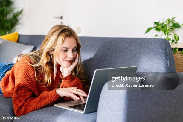 beautiful young woman at home lying on sofa using laptop computer. - rapariga no quarto tecnologia imagens e fotografias de stock