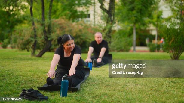 senior couple taking yoga class and stretching his body on yoga mat in public park - first gray hair stock pictures, royalty-free photos & images