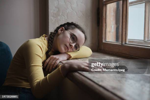 cyberbullying. upset teen girl sitting by window with mobile phone feeling depressed - female worried mobile imagens e fotografias de stock