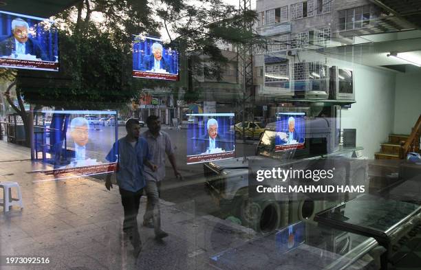 Palestinians walk past an electrical store showing Palestinian President Mahmud Abbas as he delivers a keynote speech to the central council of the...