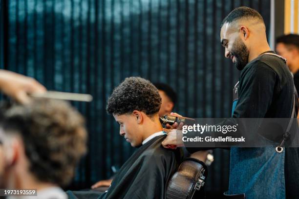 smiling barber trimming a customer's hair in a busy barber shop - barbier stockfoto's en -beelden