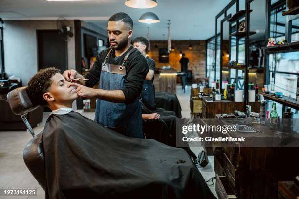 hairdresser shaping eyebrows of man client using razor in barbershop - barbers stock pictures, royalty-free photos & images