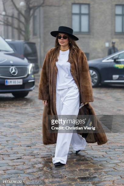 Guest wears brown fur coat, hat, white pants, Hermes bag outside Rolf Ekroth during the Copenhagen Fashion Week AW24 on January 30, 2024 in...