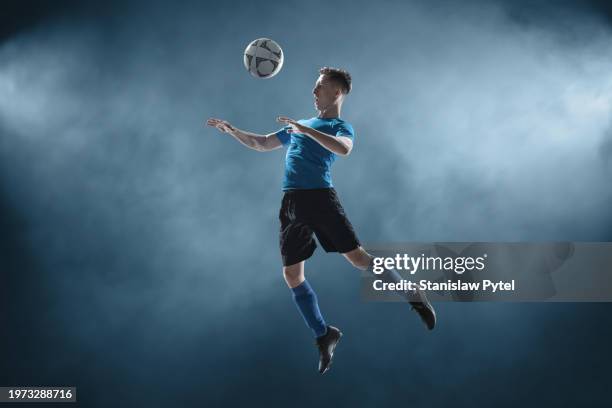 soccer player in blue outfit jumping to ball against blue smoky background - part of a series stock pictures, royalty-free photos & images