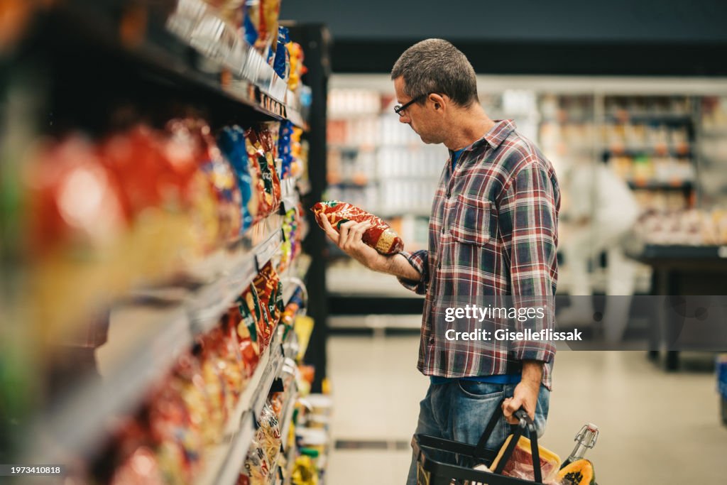 Man reading a label while grocery shopping in a supermarket aisle