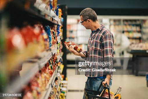 Man reading a label while grocery shopping in a supermarket aisle Man reading a label while grocery shopping in a supermarket aisle