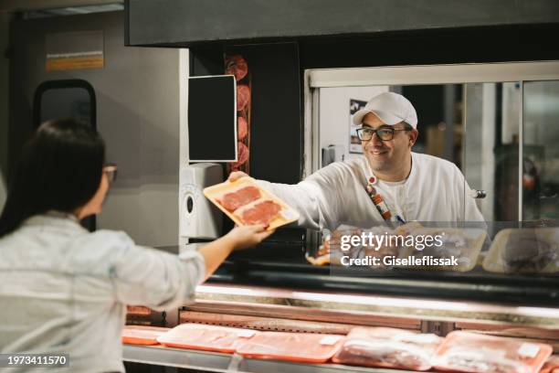 vendedor amable que entrega un paquete de carne a una clienta en la tienda de comestibles - carnicero fotografías e imágenes de stock