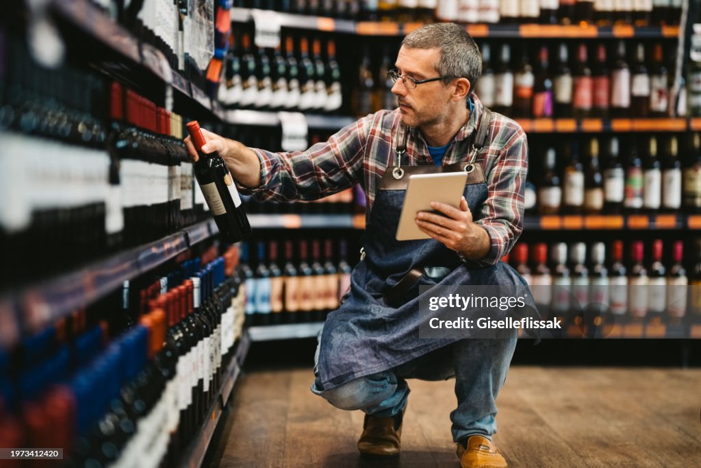 Mature salesman taking stock at supermarket wine section