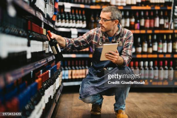 mature salesman taking stock at supermarket wine section - wine bottle stock pictures, royalty-free photos & images