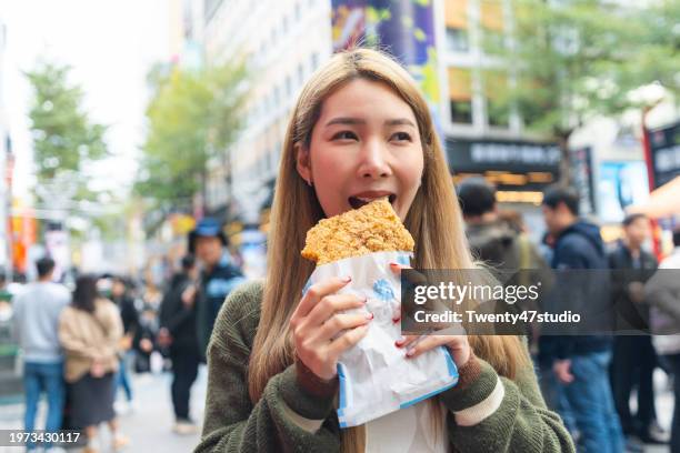 a woman eating a famous taiwanese fried chicken in ximending walking street - taiwanese culture stock pictures, royalty-free photos & images